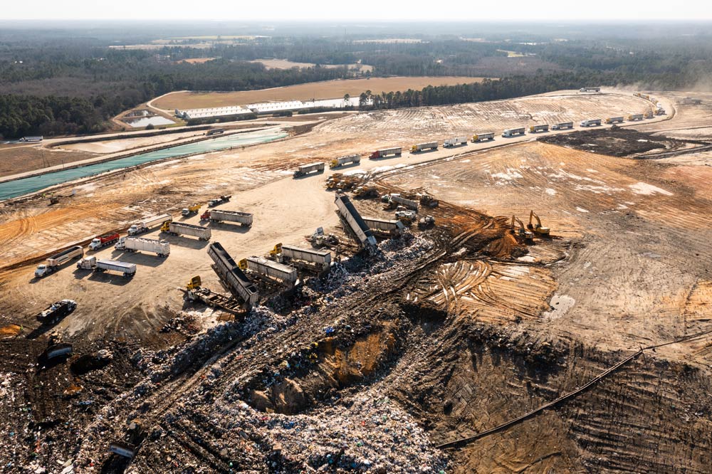 Aerial view of a large. muddy landfill complex, with dozens of trailers lined up to add their loads to the vast swath of trash crossing the landscape.