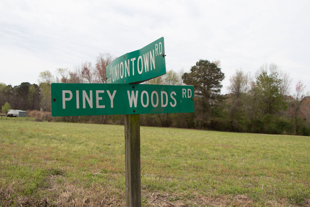 Close-up of a green street sign at a rural crossroads, The sign for one road reads Uniontown Rd and the other Piney Woods Rd.